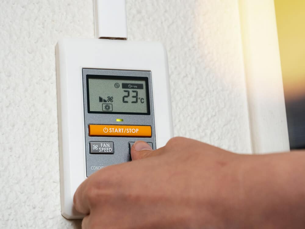 A man's hand inspecting a wall-mounted thermostat.