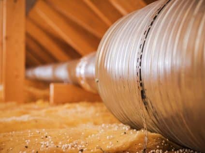 Metal ducting is placed in an attic with insulation around it for air circulation.