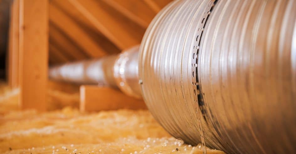 Metal ducting is placed in an attic with insulation around it for air circulation.