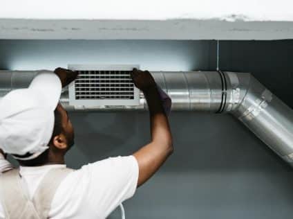 A skilled technician is installing an air duct in a residential setting, focusing on precise adjustments. The workspace is well-lit, highlighting the installation process.