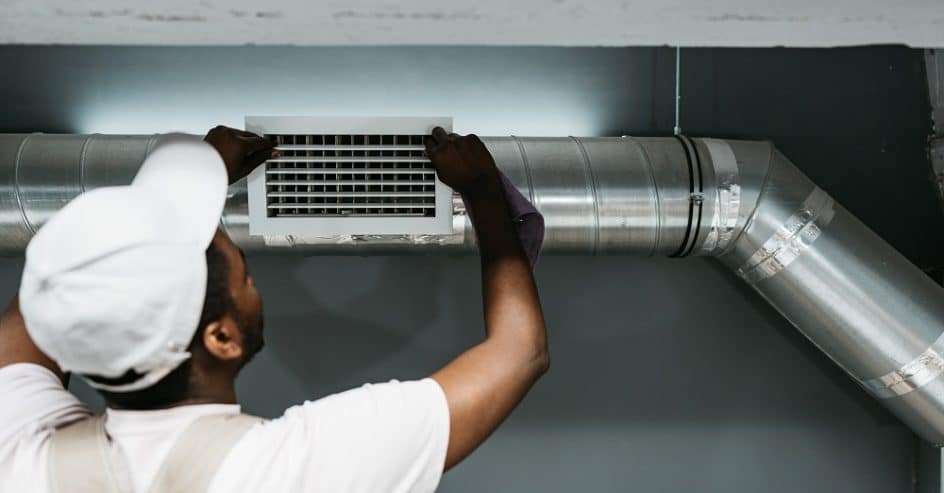 A skilled technician is installing an air duct in a residential setting, focusing on precise adjustments. The workspace is well-lit, highlighting the installation process.