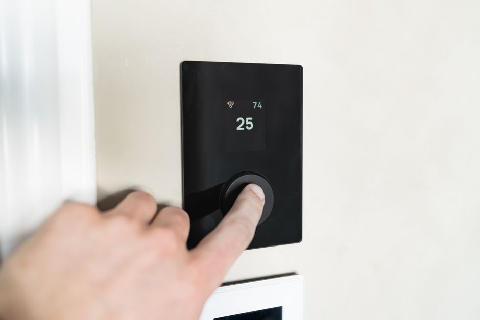 Hand resting on the dial of a black digital wall thermostat showing a set temperature