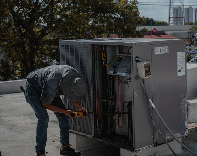Technician using a power tool to service the open side panel of an outdoor air conditioning condenser