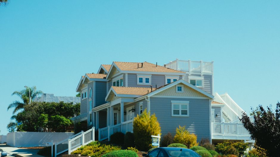 Pale blue two storey home with a garden and balcony under a clear sky