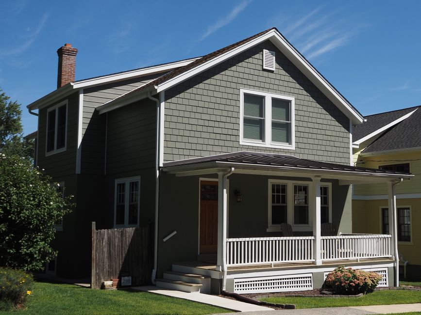 Two storey home with a covered front porch and grey shingle siding on a clear day