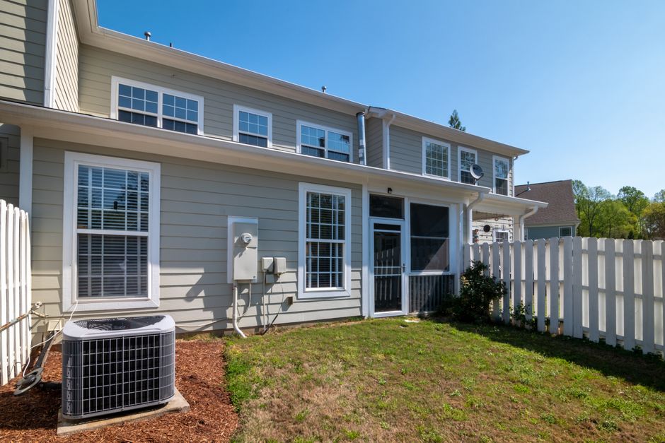 Two storey home with pale siding, a white picket fence and an outdoor air conditioning condenser beside the wall